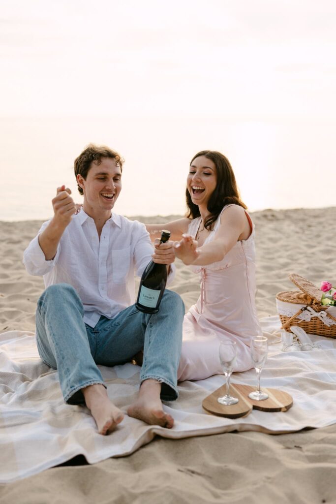 couple popping champagne for their engagement session on lake michigan