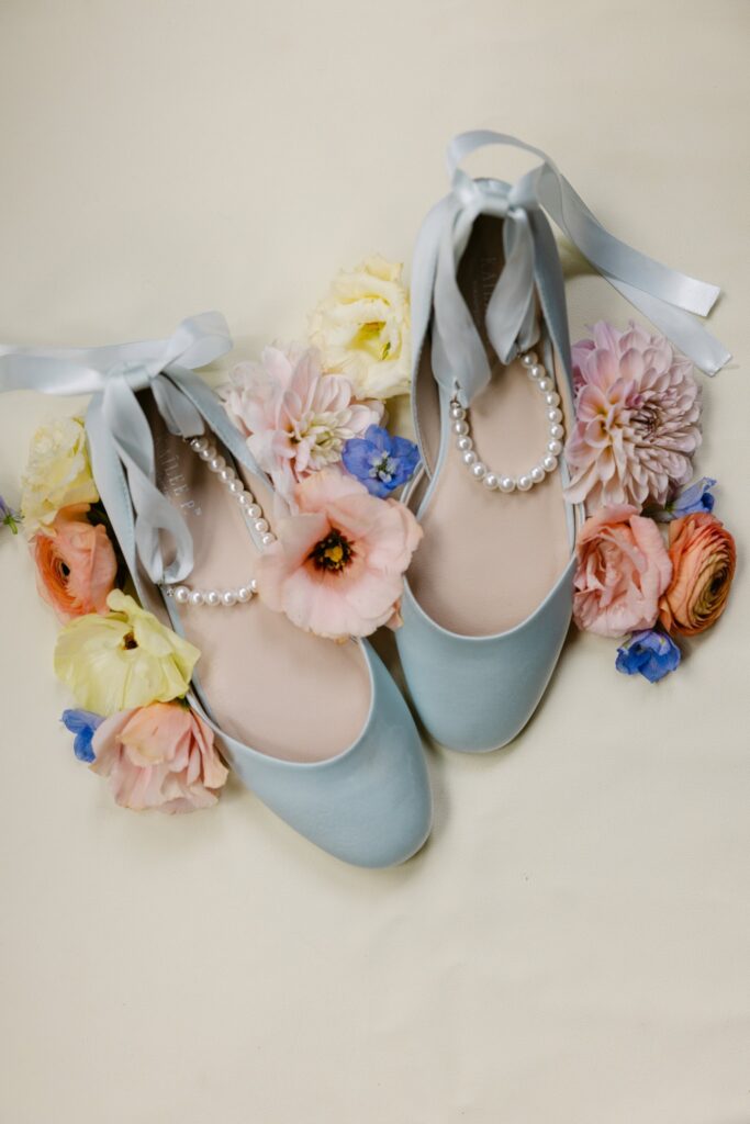 Brides blue flat shoes with pearl ankle bracelet and silk ribbon bows surrounded by flower blooms